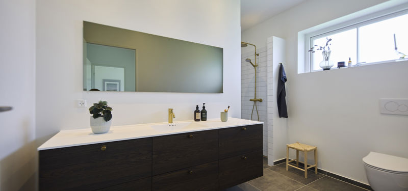 Moderne badeværelse i udstillingshus fra eurodan-huse med mørkt badmøbel, stor spejlvæg, bruseniche og lyse detaljer, der giver inspiration til nybyggeri og husdrømme.