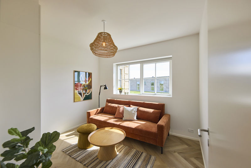 Hyggelig stue i udstillingshus fra eurodan-huse med orange sofa, rundt sofabord, sildebensgulv og stort vindue, der giver stærk inspiration til nybyggeri, husbyggeri og indretning af opholdsrum i et nyt familiehus.