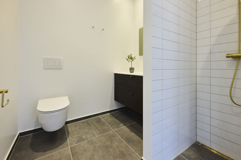 Moderne badeværelse i udstillingshus fra eurodan-huse med væghængt toilet, mørke klinker, bruseniche og gyldne armaturer, der giver inspiration til stilrent nybyggeri.