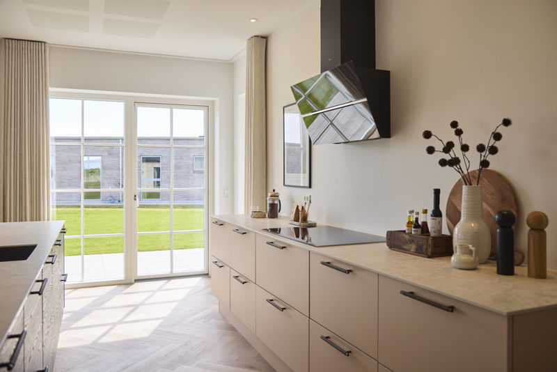 Moderne køkken i udstillingshus fra eurodan-huse med lyse køkkenfronter, sort emhætte, store terrassedøre og kig til haven, der inspirerer til nybyggeri, husbyggeri og indretning af et lyst køkkenalrum i et nyt familiehus.