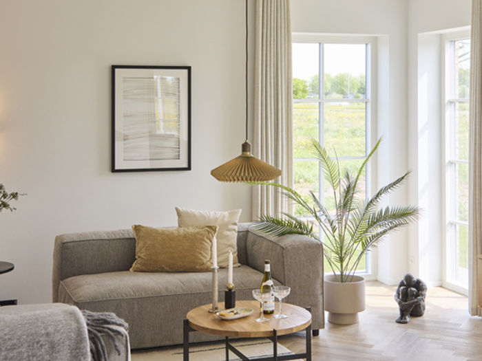 Lyst opholdshjørne i udstillingshus fra eurodan-huse med sofa, sofabord, store vinduespartier og grøn plante, der inspirerer til moderne nybyggeri, husbyggeri og hyggelige opholdsrum i et nyt familiehus.