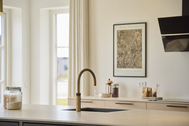 Detalje fra køkken i udstillingshus fra eurodan-huse med køkkenø, messingarmatur, lyse bordplader og moderne materialevalg, der giver inspiration til nybyggeri, husbyggeri og indretning af et stilrent køkkenalrum.