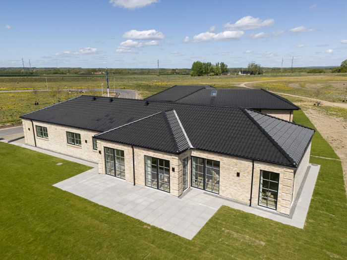 Udstillingshus fra eurodan-huse set fra luften med lys murstensfacade, sort tegltag, store vinduespartier og terrasse, der giver stærk SEO-relevant inspiration til nybyggeri, husbyggeri og drømmen om et nyt familiehus.