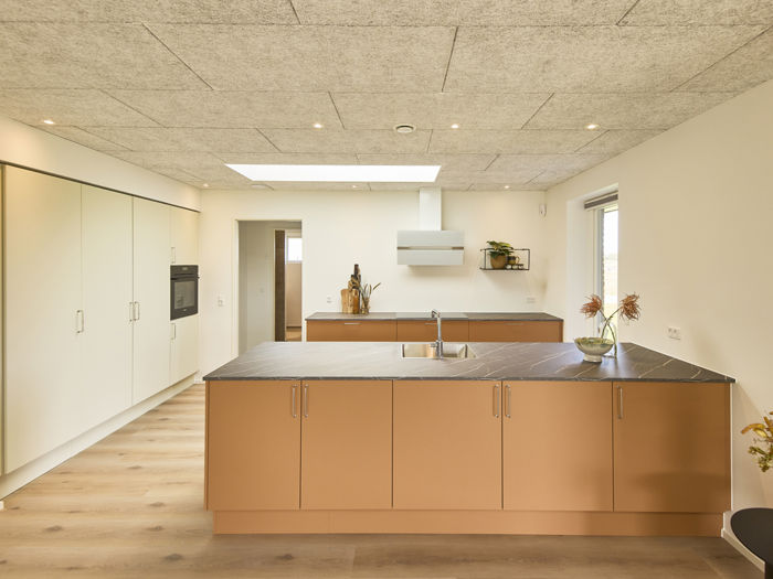 Køkken i nybygget udstillingshus fra eurodan-huse med stor køkkenø, varme terracottafarvede fronter, mørk bordplade, ovenlys og integrerede skabe som inspiration til moderne husbyggeri