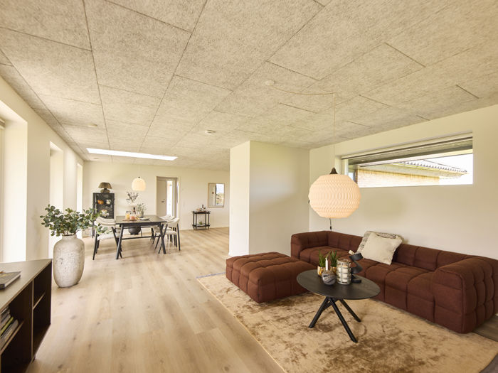Stue i nybygget udstillingshus fra eurodan-huse med brun modulsofa, akustikloft, stort vinduesparti og åben forbindelse til spiseområde som inspiration til moderne husbyggeri og husdrømme