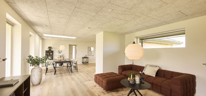 Stue i nybygget udstillingshus fra eurodan-huse med brun modulsofa, akustikloft, stort vinduesparti og åben forbindelse til spiseområde som inspiration til moderne husbyggeri og husdrømme