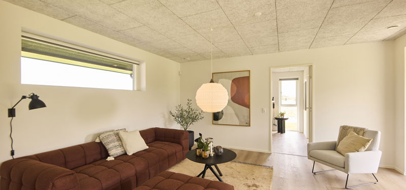 Stue i nybygget udstillingshus fra eurodan-huse med brun modulsofa, akustikloft, smalt vindue, lænestol og åben adgang til resten af boligen som inspiration til moderne husbyggeri og husdrømme