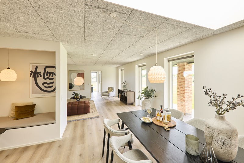 Lyst spiseområde i nybygget udstillingshus fra eurodan-huse med akustikloft, langbord, store vinduer og åben forbindelse til stue og hyggekrog for moderne husdrømme