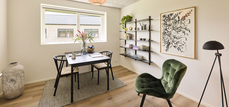 Kontor fra eurodan-huse med sort skrivebord, to sorte stole, reolvæg med bøger og pynt, grøn loungestol, gulvlampe, stort vægbillede og bredt vindue – inspiration til hjemmekontor i nybyggeri og funktionelt husbyggeri.