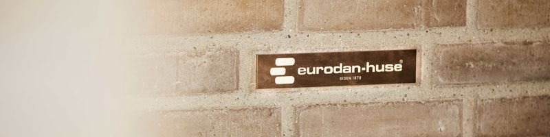 eurodan-huse-logo monteret på en lys murstensvæg i et nybygget hus