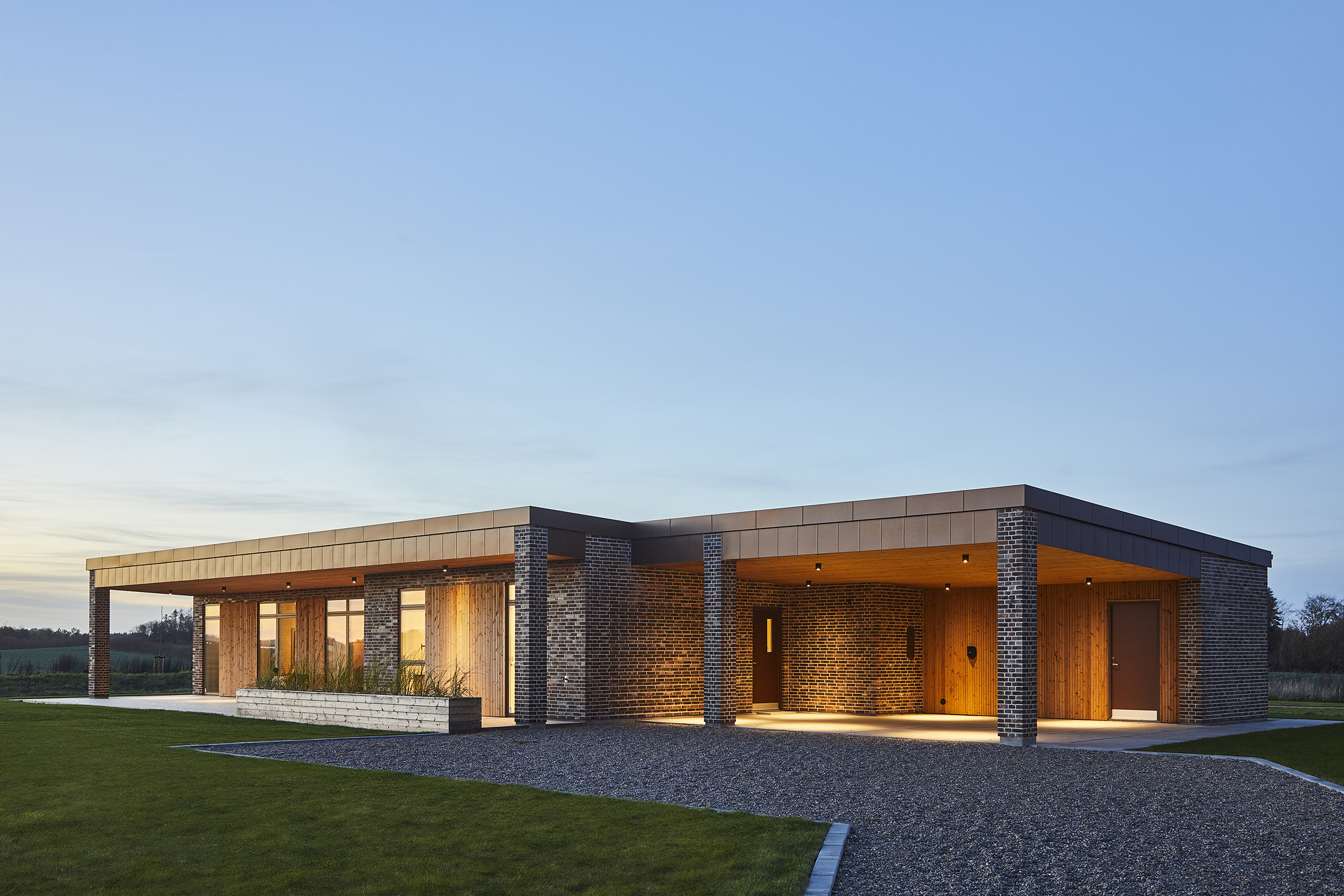 Eksklusivt udstillingshus fra eurodan-huse med træfacade, mørke murstensdetaljer, fladt tag, overdækket indgang og stemningsfuld udendørsbelysning, der inspirerer til arkitektonisk nybyggeri, moderne husbyggeri og unikke husdrømme i et nyt familiehus.