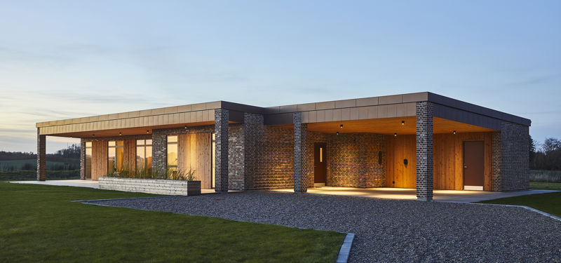 Eksklusivt udstillingshus fra eurodan-huse med træfacade, mørke murstensdetaljer, fladt tag, overdækket indgang og stemningsfuld udendørsbelysning, der inspirerer til arkitektonisk nybyggeri, moderne husbyggeri og unikke husdrømme i et nyt familiehus.