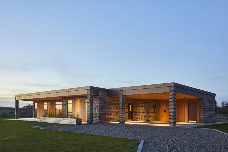 Eksklusivt udstillingshus fra eurodan-huse med træfacade, mørke murstensdetaljer, fladt tag, overdækket indgang og stemningsfuld udendørsbelysning, der inspirerer til arkitektonisk nybyggeri, moderne husbyggeri og unikke husdrømme i et nyt familiehus.