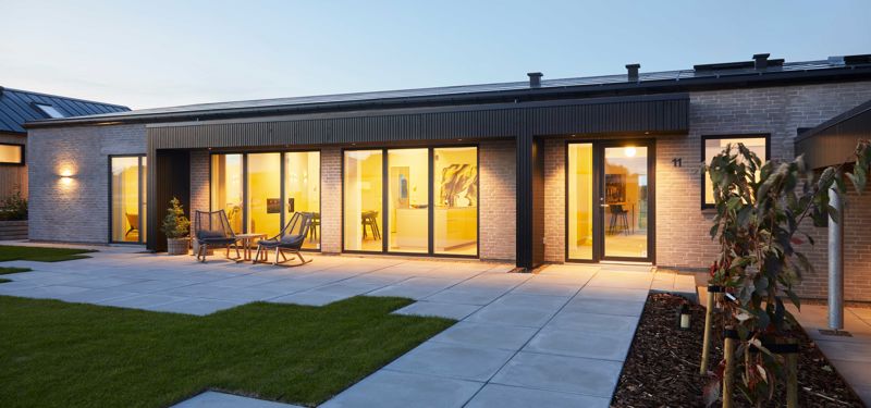 Moderne længehus i nybyggeri med store vinduespartier, oplyste opholdsrum, flisebelagt terrasse og anlagt have.