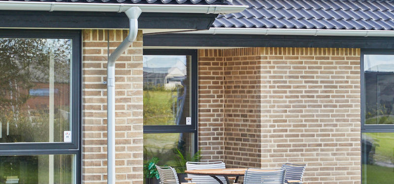 Overdækket terrasse ved murstenshus fra eurodan-huse med havemøbler, store vinduespartier og solceller på taget, der giver inspiration til moderne nybyggeri.