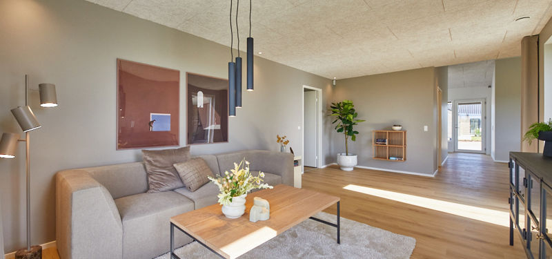 Stue i nybygget udstillingshus fra eurodan-huse med lys sofa, akustikloft, trægulv, sofabord og åben forbindelse til entré som inspiration til moderne husbyggeri og husdrømme