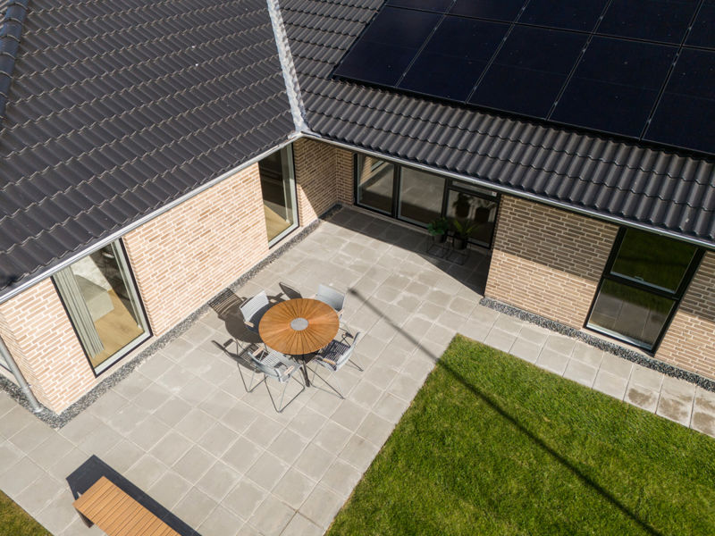 Overdækket terrasse i nybygget udstillingshus fra eurodan-huse med grå fliser, havemøbler, sort tegltag, solceller og grøn have som inspiration til moderne husbyggeri og husdrømme