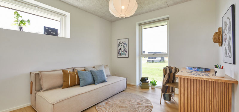 Lyst multirum i udstillingshus fra eurodan-huse med daybed, skrivebord og store vinduer, der viser mulighederne for fleksible rum i nybyggeri.