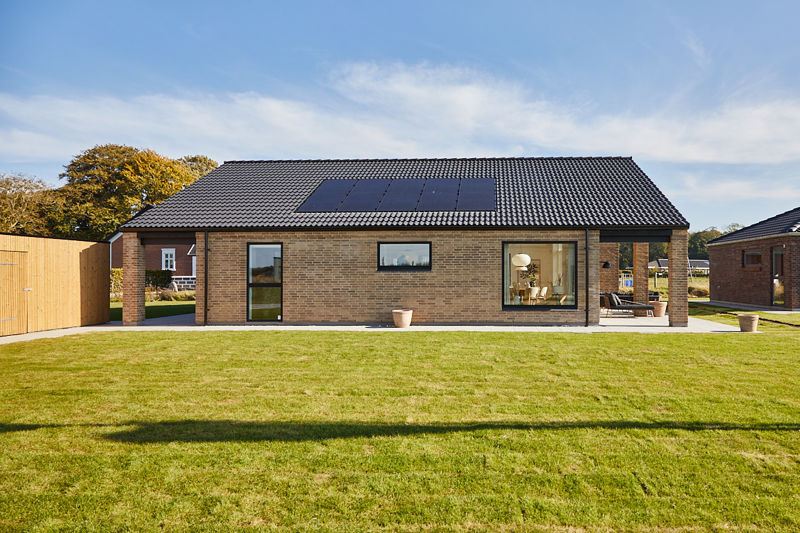 Husbyggeri med moderne længehus, solceller på sort tag, store vinduer og overdækket terrasse til husdrømme