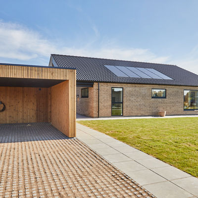 Nybyggeri fra eurodan-huse med murstensfacade, sort tag, solceller og træbeklædt carport ved moderne længehus