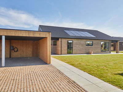 Nybyggeri fra eurodan-huse med murstensfacade, sort tag, solceller og træbeklædt carport ved moderne længehus