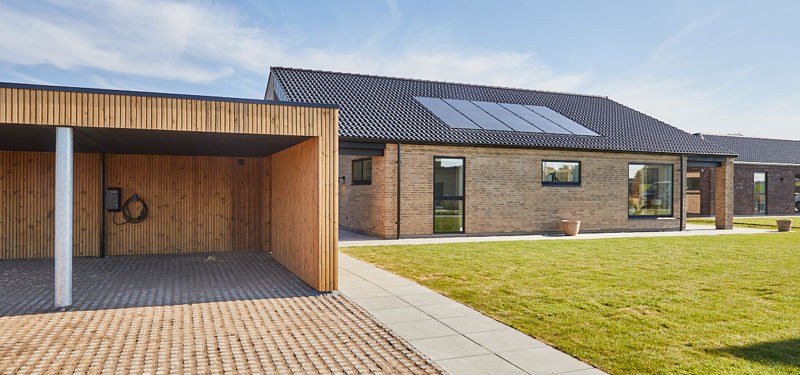 Nybyggeri fra eurodan-huse med murstensfacade, sort tag, solceller og træbeklædt carport ved moderne længehus