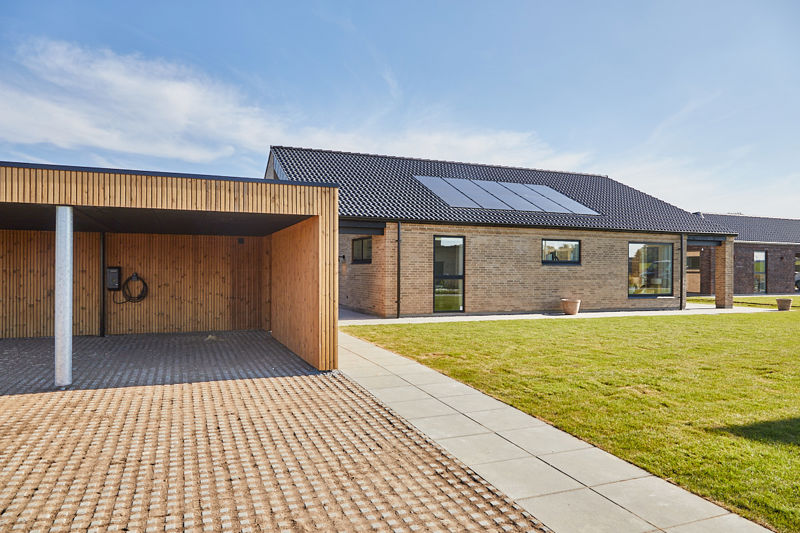 Nybyggeri fra eurodan-huse med murstensfacade, sort tag, solceller og træbeklædt carport ved moderne længehus