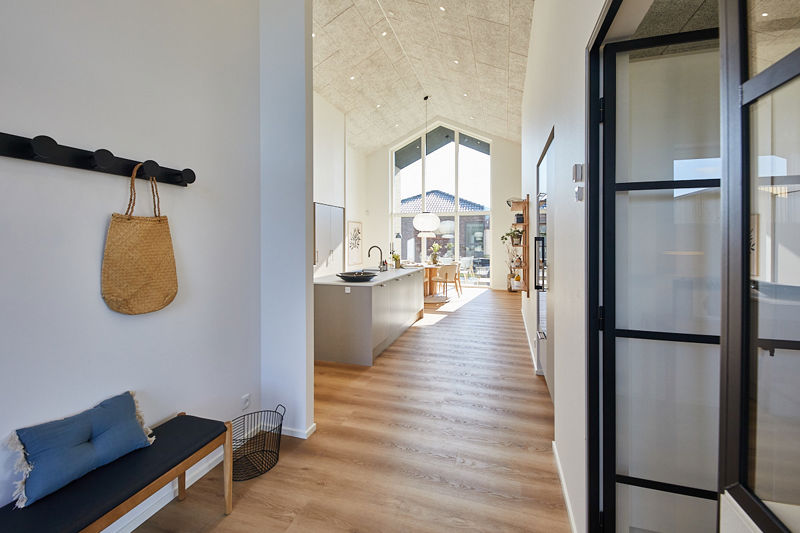 Lys entré fra eurodan-huse med sort knagerække, bænk med blå hynde, kurv til opbevaring, sort rammedør mod kontor og langt kig ind i åbent køkken-alrum med store vinduespartier – inspiration til moderne nybyggeri og gennemtænkt husbyggeri.