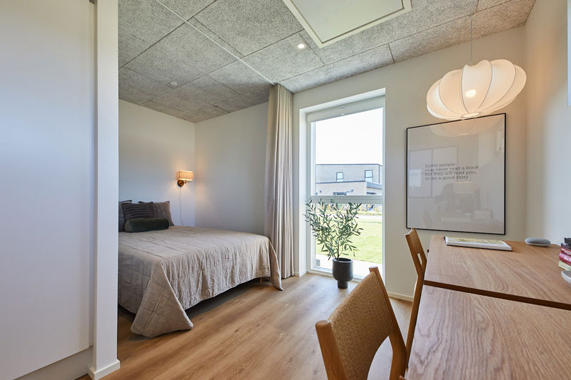 Hyggelig stue i husbyggeri med lys sofa, akustikloft, moderne pendel og rolig indretning