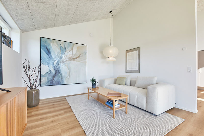 Hyggelig stue i husbyggeri med lys sofa, akustikloft, moderne pendel og rolig indretning