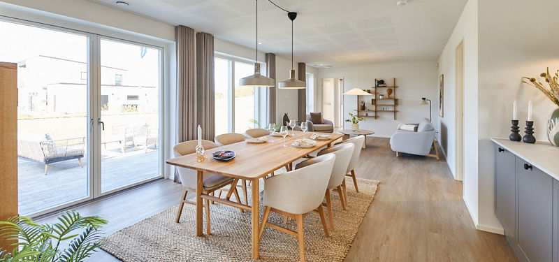 Rummeligt køkken-alrum i nybyggeri med spiseplads, gulv-til-loft vinduer, terrasseadgang og naturligt lys til moderne familieliv