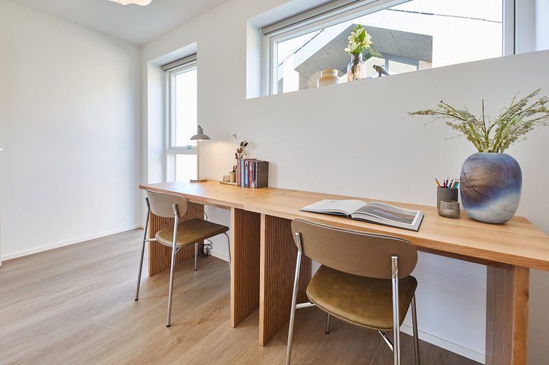 Kontorplads i nybyggeri med langt skrivebord, to arbejdsstationer, høje vinduer og lys indretning til fleksible husdrømme