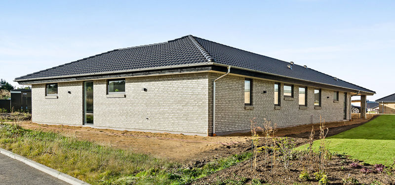 Nyt hus fra eurodan-huse med lyse mursten, sort valmtag, smalle vinduer og nyanlagt have omkring boligen.