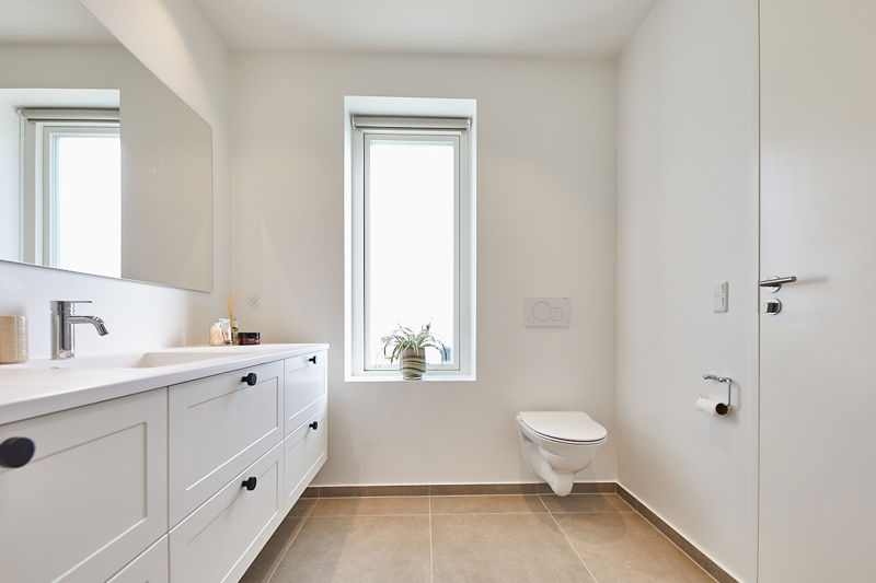 Lyst badeværelse i nybygget hus med væghængt toilet, bredt vaskemøbel, stort spejl og vindue med dagslys fra eurodan-huse