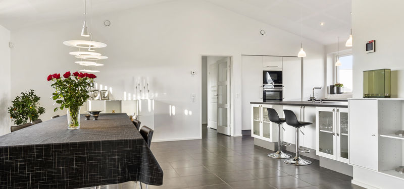 Rummeligt køkken-alrum fra eurodan-huse med loft til kip, lang spiseplads, mørke gulvfliser og hvid køkkenø til moderne husdrømme.