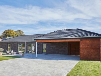 Nybyggeri og husbyggeri med moderne længehus i brunlige mursten, sort tag, træbeklædt carport og overdækket indkørsel fra eurodan-huse