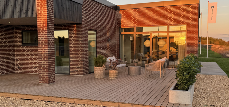 Overdækket terrasse ved nybygget funkishus fra eurodan-huse med træterrasse, teglfacade og aftenlys