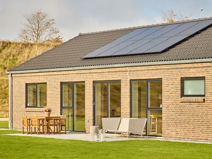 Nybyggeri med solcelleanlæg på sort tegltag, lyse mursten, store vinduer og terrasse som viser moderne husdrømme fra eurodan-huse