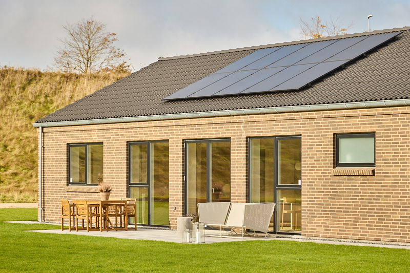 Nybyggeri med solcelleanlæg på sort tegltag, lyse mursten, store vinduer og terrasse som viser moderne husdrømme fra eurodan-huse