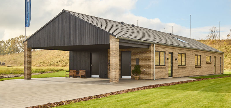 Moderne længehus i nybyggeri med sort tag, lyse mursten, mørk træbeklædt carport og enkel arkitektur til familiens husdrømme