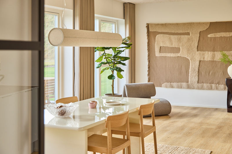 Husdrømme med lys spiseplads, moderne pendel, store vinduer, grøn plante og tekstil vægdekoration i åbent køkken-alrum