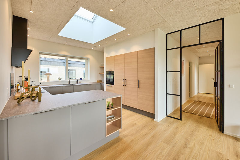 Nybyggeri med moderne køkken i grå og træ, stor køkkenø, ovenlysvindue, troltekt loft og sort New Yorker-dør mod entré