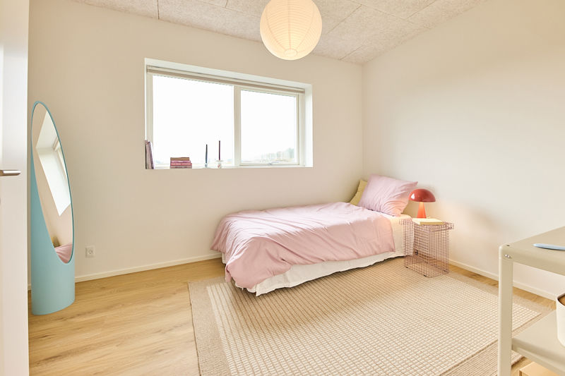 Lyst børneværelse i nybygget familievilla med rosa seng, rundt spejl, skrivebord, stort vindue og god plads til indretning