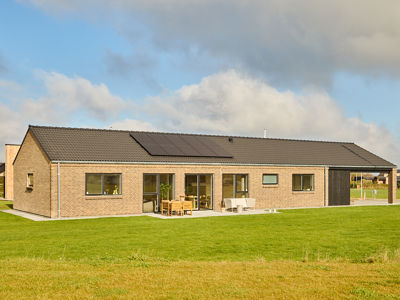 Nybyggeri med moderne lavenergi længehus i lyse mursten, sort tegltag, solcelleanlæg, integreret carport og terrasse ved grøn have