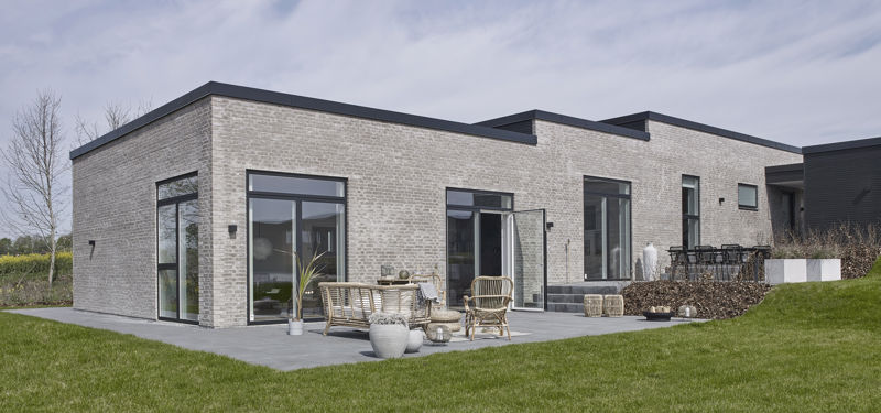 Moderne nybyggeri fra eurodan-huse med lyse mursten, fladt tag, store sorte vinduespartier og solrig terrasse med havemøbler.