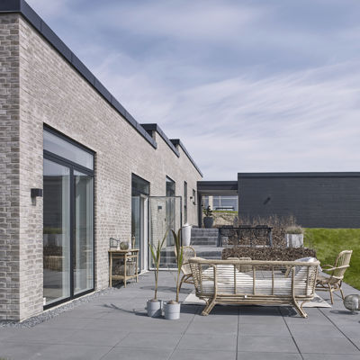 Flisebelagt terrasse ved moderne nybyggeri fra eurodan-huse med grå mursten, store vinduespartier og loungemøbler.