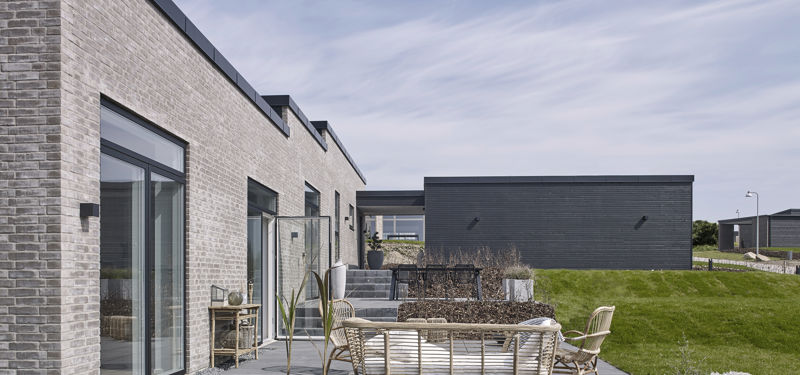 Flisebelagt terrasse ved moderne nybyggeri fra eurodan-huse med grå mursten, store vinduespartier og loungemøbler.