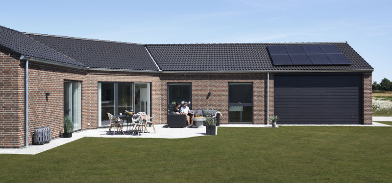 Moderne knækhus på 176 m² med rød murstensfacade, sort tegltag, solceller, integreret garage og flisebelagt terrasse ud mod den store græsplæne – inspiration til nybyg og familiens husdrømme.