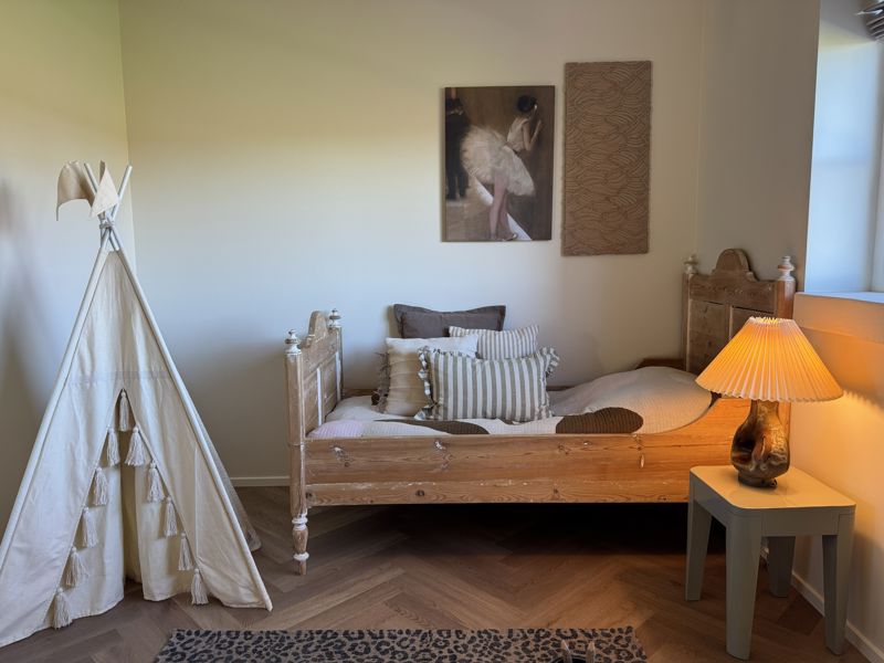 Hyggeligt børneværelse med træseng, legetelt og varme farver i et nybygget hus