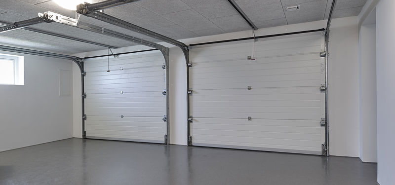 Dobbeltgarage fra eurodan-huse med to hvide ledhejseporte, blankt gråt gulv, loftmonterede portskinner, lys vægfarve og lille vindue i siden – konkret inspiration til lukket garage, praktisk opbevaring og moderne nybyggeri.